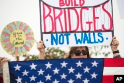 FILE - A protester holds up a sign during a rally against a scheduled visit by President Donald Trump, in San Diego, California, March 13, 2018.