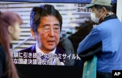 FILE - Passers-by look at a TV screen showing Japanese Prime Minister Shinzo Abe. Many feel Abe's 'Abenomics' policies have not done enough for the economy.