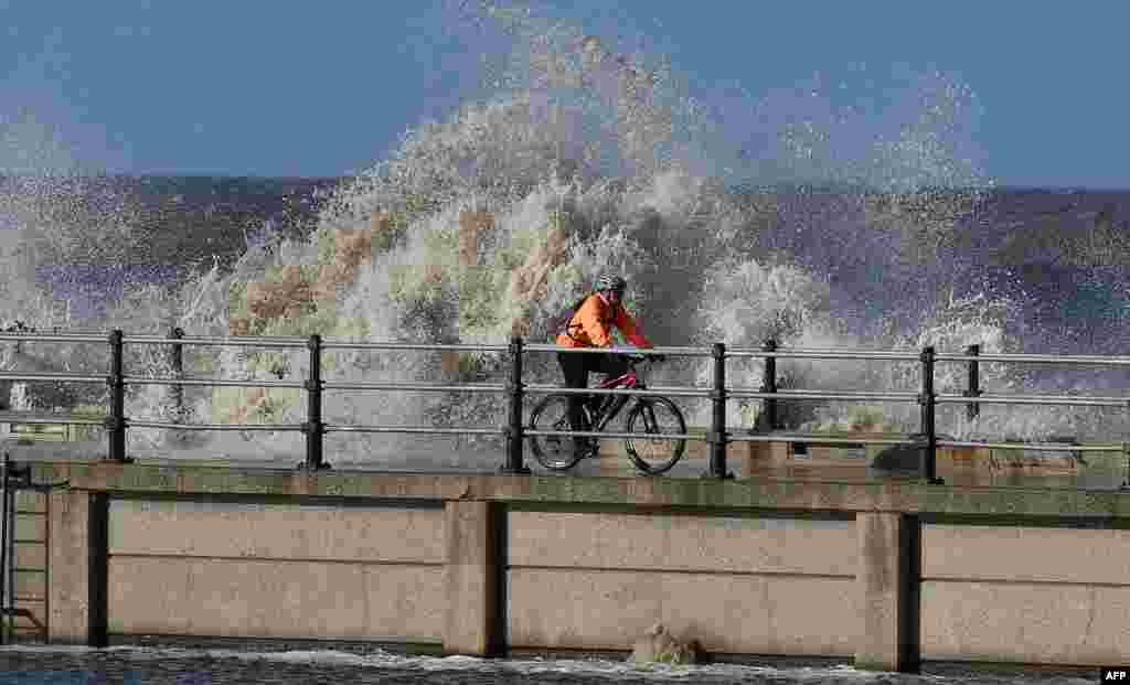A man cycles on the path between the marine lake and the coastal wall at New Brighton, north west England as waves from the Irish Sea hit the coast.