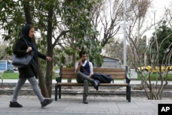 Amir Ali Najafi, a transgender man, talks on his cellphone as a woman walks on a sidewalk in downtown Tehran, Iran, March 11, 2018.