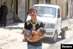 A civilian evacuates a baby from a site hit by airstrikes in the rebel-held area of Aleppo's al-Fardous district, Syria, April 29, 2016.