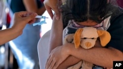 A girl hugs her stuffed toy as she gets a shot of the Pfizer COVID-19 vaccine at a community health center, in Brasilia, Brazil, Jan. 16, 2022.