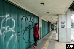 Seorang pria berjalan melewati toko-toko yang sepi setelah penerapan Pembatasan Sosial Berskala Besar (PSBB) di Jakarta, 10 April 2020. (Foto: AFP)