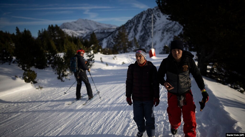 A person skiing, a mountain sport, passes by Afghan migrants Sayed Hamza, left, and Ali Rezaie as they make the crossing through the French-Italian Alps to reach a migrant center in Briançon, France on December 12, 2021. (AP Photo/Daniel Cole)