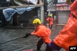 Fire rescue members prepare a rope to help people cross a flooded street at the village of Lei Yu Mun during Typhoon Mangkhut in Hong Kong, Sept. 16, 2018.