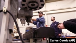 In a photo from Wednesday, Feb. 11, 2015 in Lansing, Mich., Lansing Community College, Brad Bancroft, left, operates a mill as Nate Joseph, center, and Adam Woodhams, right, look on in the advanced precision machining class. (AP Photo/Carlos Osorio)