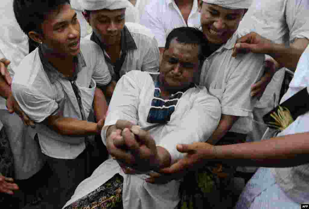 A Balinese man jabs himself with a "keris", a traditional dagger, to perform "ngurek" or a self-stabbing ritual at a temple in Kesiman, east Denpasar on the Indonesian resort island of Bali. Participants work themselves into a state of trance (out of consciousness) by dancing during the century-old sacred ceremony, then turning the keris on themselves.