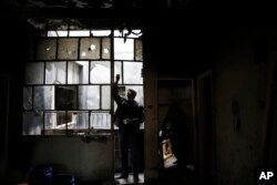 Mohammed Bayraqdar removes broken window glass at his burned house in Khaldiyeh, one of the worst damaged neighborhoods in Homs, Syria, Jan. 17, 2018.