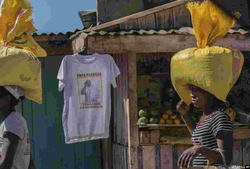 Women carrying bags on their heads pass a stall selling T-shirts of Pope Francis ahead of his visit to Madagascar next weekend, in Antananarivo, Madagascar.