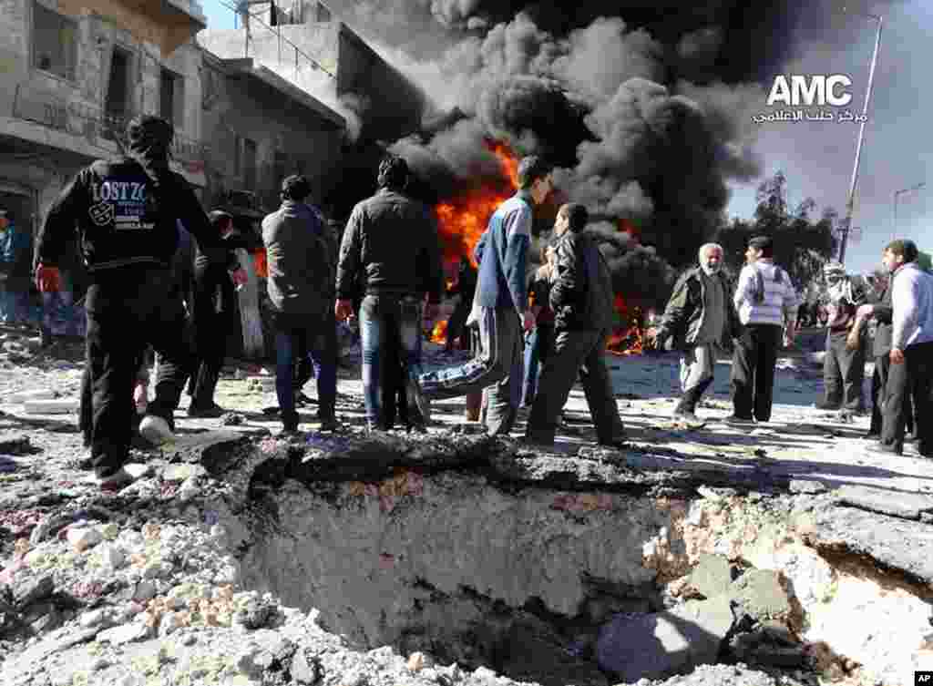 This citizen journalism image provided by the Aleppo Media Center (AMC), an anti-Bashar Assad group, shows people gathering near flames after a Syrian government forces warplane attack in al-Bab, Aleppo, Feb. 1, 2014.