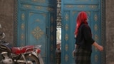 资料照：中国新疆一名维吾尔族女子走过一扇门，一个孩子正在向外张望。（2013年10月31日）