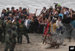 U.S. police and Border Patrol hold a line as members of an inter-faith group, showing support for Central American asylum-seekers who arrived in recent caravans and calling for an end to detaining and deporting immigrants, pray during a protest in San Diego, as seen from across the border wall in Tijuana, Mexico, Monday, Dec. 10, 2018.