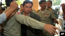Chay Sarith, center, a suspected attacker who is accused of beating two opposition lawmakers along with two others, is escorted by police officers at Phnom Penh Municipal Court in Phnom Penh, Cambodia, Wednesday, Nov. 4, 2015. 