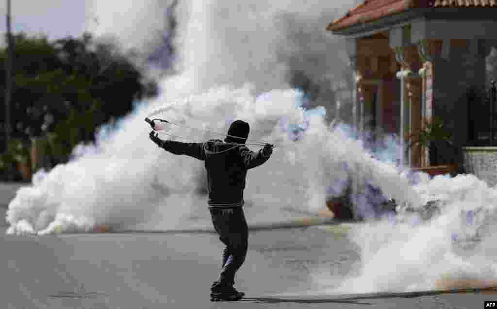 A Palestinian man uses a slingshot to throw back a tear gas canister towards Israeli soldiers during clashes in the West Bank village of Silwad, north of Ramallah.