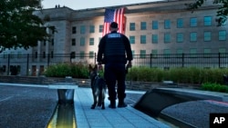 At the Pentagon Memorial, a K-9 officer pauses as he looks toward the U.S. flag as it is draped on the side of the Pentagon where the building was attacked on September 11 in 2001, on the 14th anniversary of the attack, Sept. 11, 2015, outside Washington.