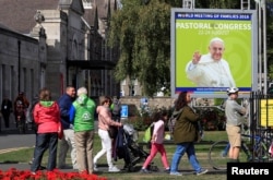 People walk past a poster of Pope Francis outside the Pastoral Congress at the World Meeting of Families in Dublin, Ireland, Aug. 24, 2018.
