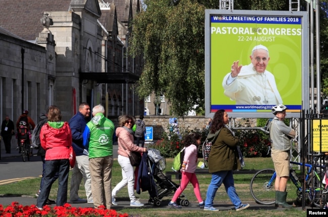 People walk past a poster of Pope Francis outside the Pastoral Congress at the World Meeting of Families in Dublin, Ireland, Aug. 24, 2018.