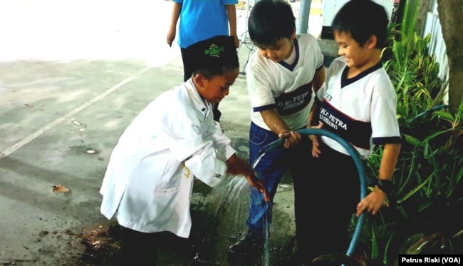 Siswa-siswi dari Madrasah Ibtidaiyah (MI) Islamiyyah-Plosogenuk, sedang mengambil air wudu sementara siswa siswi SD Kristen Petra membantu dengan memegangi selang air (Foto:VOA/Petrus Riski).