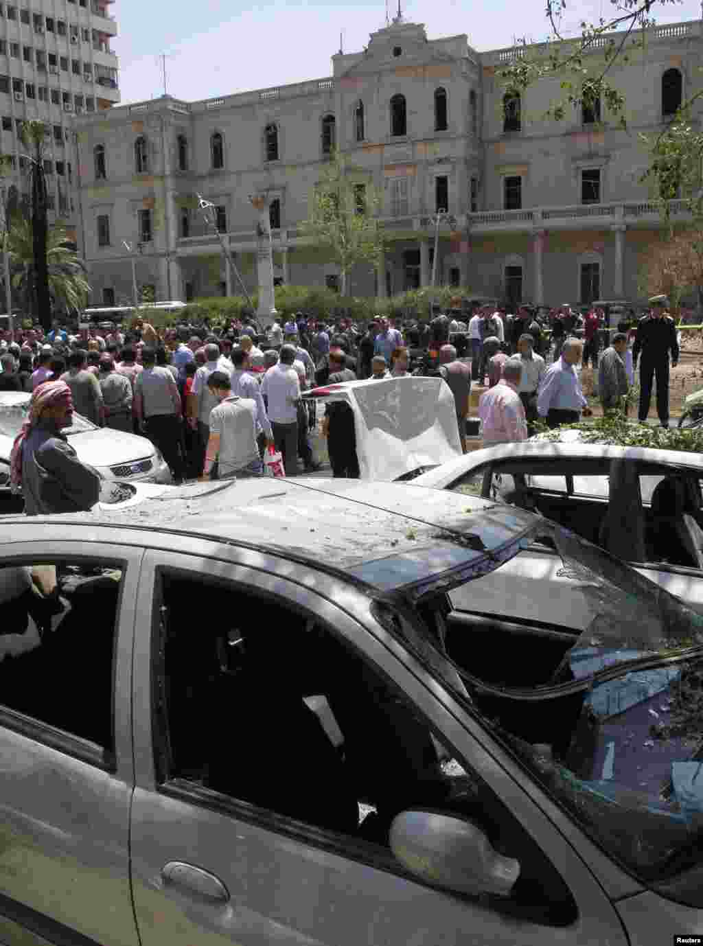 People walk on a street near the former Interior Ministry building and destroyed cars after a blast at Marjeh Square in Damascus April 30, 2013. 