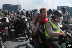 FILE - Police officers ride away on a motorcycle with a detained anti-government protester, in Caracas, Venezuela, April 24, 2017.