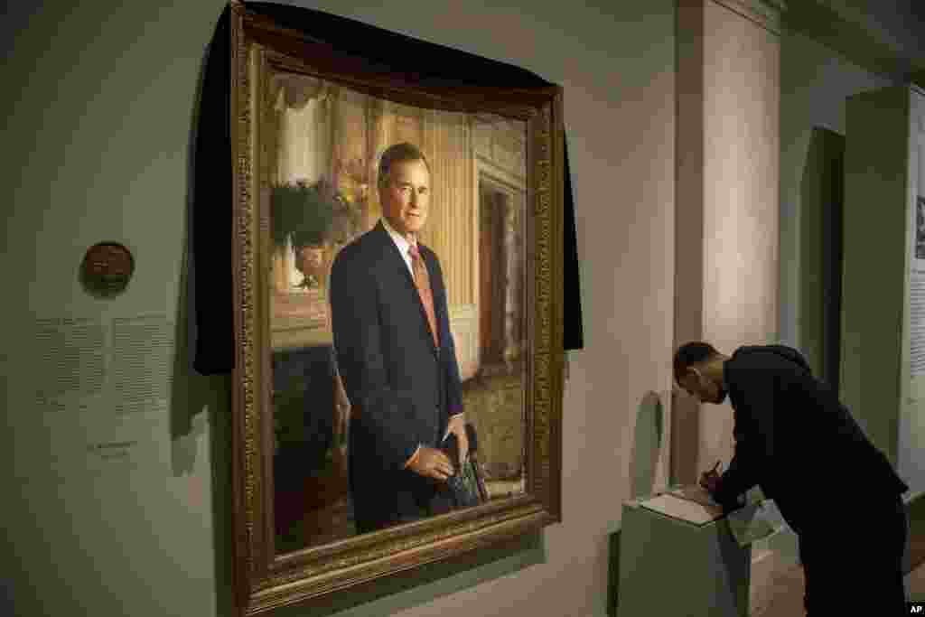 Ameer Hassan, warga New York memberikan tanda tangan tanda di buku duka cita di depan potret mendiang mantan Presiden AS George H.W. Bush yang dihiasi kain hitam tanda berkabung di National Portrait Gallery di Washington, 3 Desember 2018.