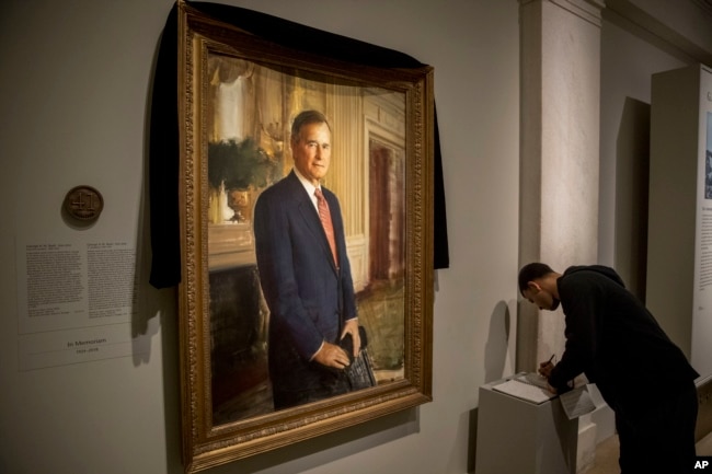 Ameer Hassan of New York stops to sign the condolence book as the official portrait of former President George H.W. Bush is draped in black cloth at the National Portrait Gallery in Washington, Dec. 3, 2018, to mark his passing. Bush will lay in state at the Capitol building this week before being buried in Texas.