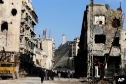 Residents walk through damaged buildings near to the ancient Aleppo Citadel, background, that government troops used as a military base in the old city of Aleppo, Syria, Jan. 21, 2017.