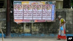 A Sri Lankan woman walks past a notice board covered with posters carrying portraits of President Maithripala Sirisena and newly appointed Prime Minster Mahinda Rajapaksa at a street in Colombo, Sri Lanka, Sunday, Oct. 28, 2018.