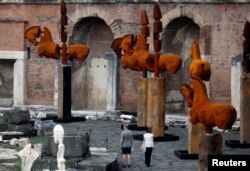 People visit the sculptures of horses by Mexican artist Gustavo Aceves at Fori Imperiali (The Imperial Fora) during an exhibition called "Lapidarium, Waiting for the Barbarians" in Rome, Italy, Sept. 15, 2016.