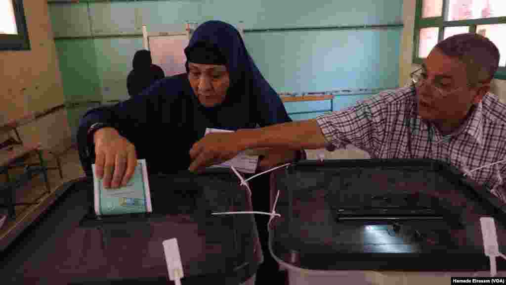 Petugas tempat pemungutan suara membantu seorang pemilih memasukkan kertas suaranya dalam kotak yang benar dalam pemilihan parlemen di Giza, Mesir (18/10).