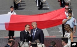 French President Emmanuel Macron talks with President Donald Trump next to a huge French flag after the Bastille Day parade in Paris, July 14, 2017.