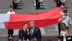 French President Emmanuel Macron talks with President Donald Trump next to a huge French flag after the Bastille Day parade in Paris, July 14, 2017. 