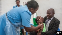 FILE - A health worker administers a typhoid vaccine dose to a boy, as his father holds him, during a typhoid vaccination drive at Ndirande Health Centre in Blantyre, Malawi, Feb. 21, 2018.