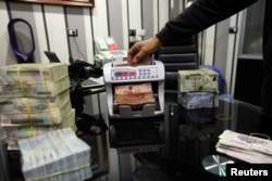 A man uses a currency counting machine to count Libyan dinars at a currency exchange office in Tripoli, April 27, 2016.