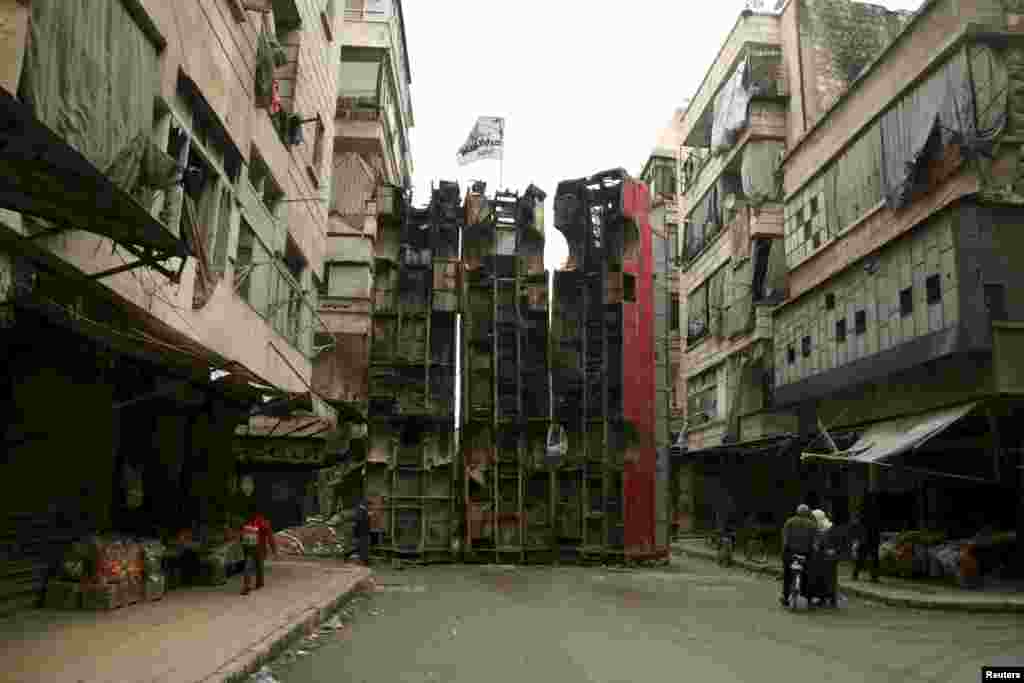 Civilians walk near upright buses barricading a street as protection from snipers loyal to Syria&#39;s President Bashar al-Assad in Aleppo&#39;s rebel-controlled Bustan al-Qasr neighbourhood.