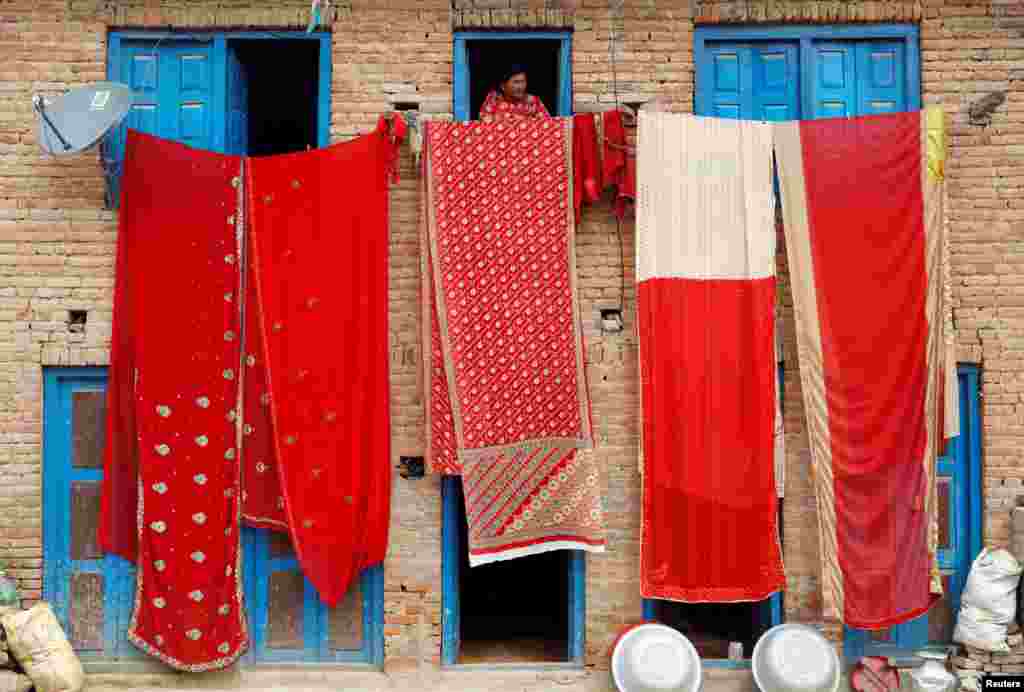 A woman looks out of the window of a house as saris, traditional clothing worn by women, are hung out to dry, in Lalitpur, Nepal.