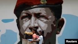 Women walk past a portrait of Venezuela's late President Hugo Chavez in Caracas, Venezuela August 7, 2017. 
