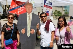 FILE - After their citizenship ceremony, recently naturalized U.S. citizens pose with a cutout of President Donald Trump at a Republican Party voter registration booth in Los Angeles, July 18, 2017.