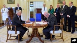 Commissioner Justice Peter McClellan, seated left, watches as Governor-General of Australia Peter Cosgrove, seated right, signs a document after receiving the final report of the Royal Commission into Institutional Responses to Child Sexual Abuse at Government House, in Canberra, Dec. 15, 2017. 