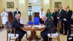 FILE - Commissioner Justice Peter McClellan, seated left, watches as Governor-General of Australia Peter Cosgrove, seated right, signs a document after receiving the final report of the Royal Commission into Institutional Responses to Child Sexual Abuse at Government House, in Canberra, Dec. 15, 2017.