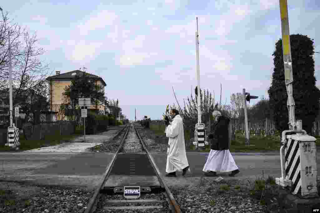 Priests Don Giuseppe Arnaudo (R), and Don Kresimir Busic, holding a crucifix, cross railway tracks as they conduct a countryside procession to bless houses against the coronavirus pandemic, March 25, 2020 in Manta, near Cuneo, northwestern Italy.