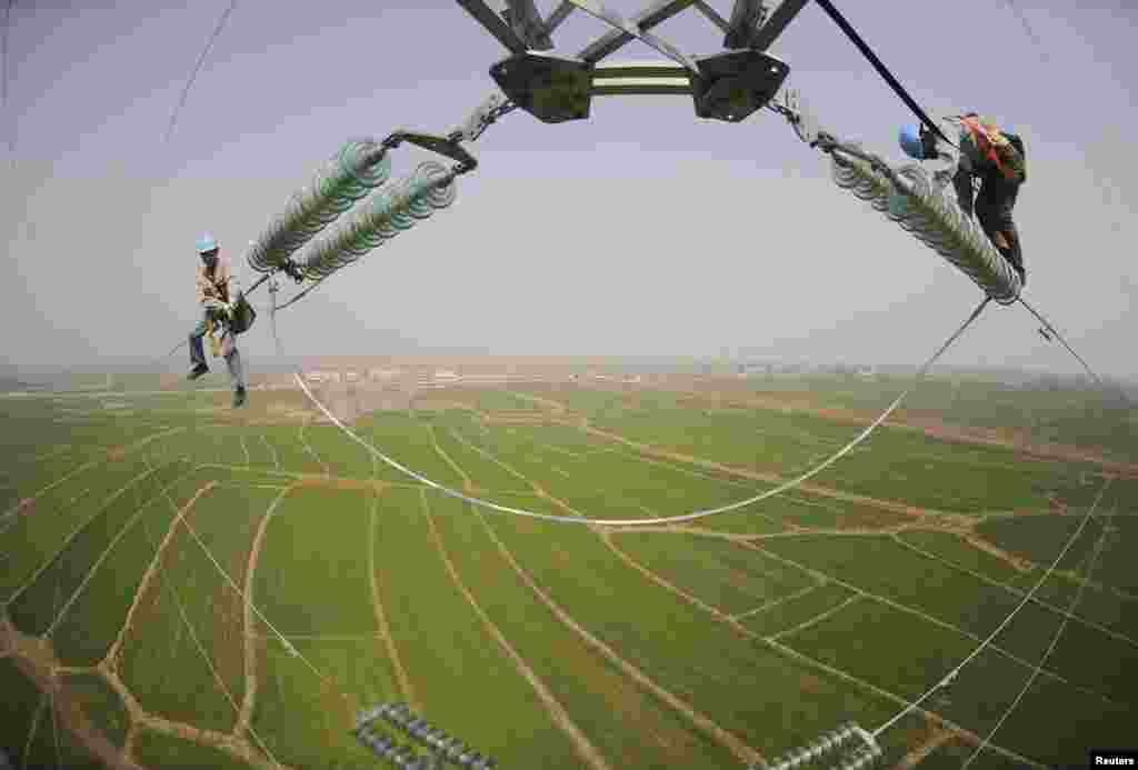 Dua orang teknisi memeriksa tiang listrik yang terletak di tengah lahan pertanian di Chuzhou, provinsi Anhui, China.