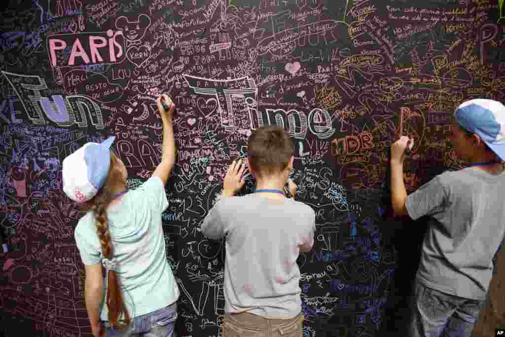 Anak-anak membubuhkan nama mereka dan menggambar di sebuah papan dinding dalam acara Vacation for Everyone di Menara Eiffel di Paris, Perancis.