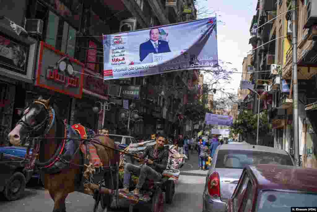 A carriage passes a street sign, March 8, 2018, in downtown Cairo in support of President Abdel Fattah el-Sissi’s second term. It says, in Arabic, “we will satisfy ourselves to be ourselves decision makers.” Sissi is running largely unopposed.