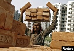 FILE - A laborer stacks bricks on his head at the construction site of a residential complex in Kolkata, Feb. 28, 2015.