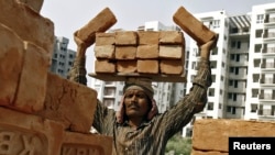  FILE - A laborer stacks bricks on his head at the construction site of a residential complex in Kolkata.