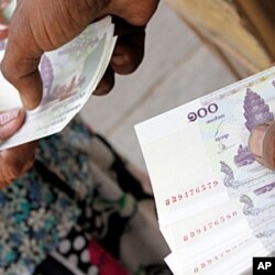 ພະນັກງານທີ່ຮ້ານແລກປ່ຽນເງິນຕາແຫ່ງ ນຶ່ງ ຈ່າຍເງິນໃບ 100 ຫລຽນຂະເໝນ ໃຫ້ລູກຄ້າທີ່ນະຄອນຫລວງພະນົມເປັນ, ວັນທີ 12 ມີນາ 2011. (file photo)