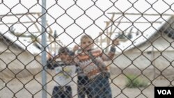 Children peer out from behind the fence at Schisto camp. Refugees are free to come and go as they like at the camp, but many feel trapped by the slow, uncertain process of relocating to elsewhere in Europe, or seeking asylum in Greece. (J. Owens for VOA)