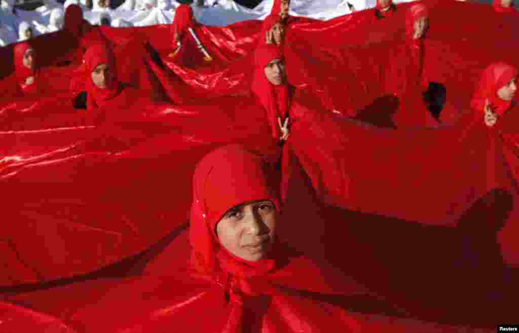 Girls appear through holes in a big national flag as they prepare to take part in a parade commemorating the second anniversary of the uprising against Yemen&#39;s former president Ali Abdullah Saleh in Sanaa. 
