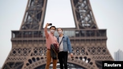 Pengunjung mengenakan masker wajah melakukan selfie di alun-alun Trocadero dekat Menara Eiffel, di Paris, saat Perancis mulai secara bertahap mengakhiri lockdown secara nasional di tengah pandemi Covid-19, 16 Mei 2020.